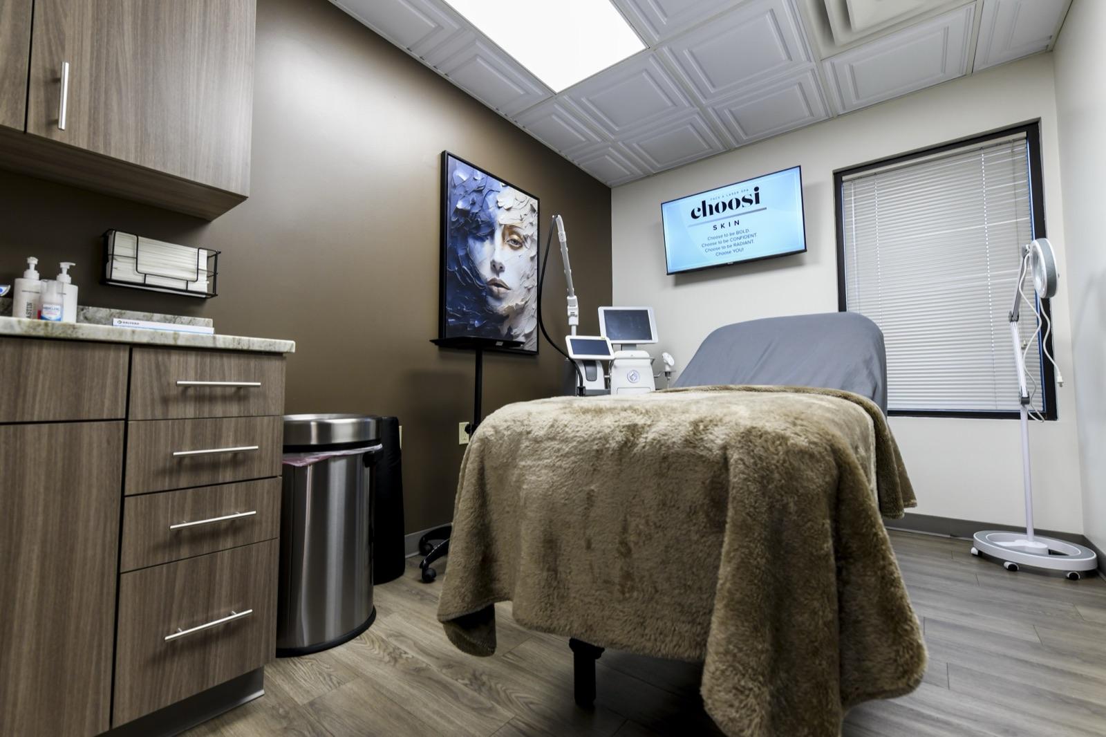A Choosi treatment room, laser console and monitor beside the bed with the brand screen lit on the wall